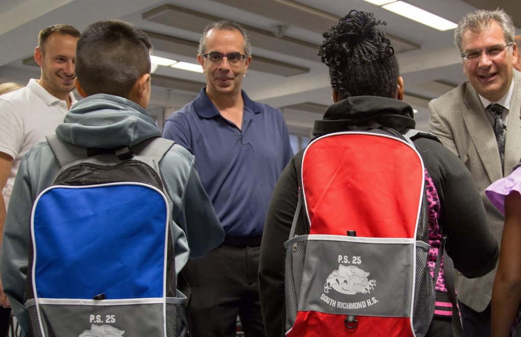 From left, Realtors Kevin Swetsky and Mike Gentilesco work with Assistant Principal Anthony Casella in distributing SIBOR Pack To School supplies in 2015 to students at PS 25/South Richmond High School in Staten Island, N.Y